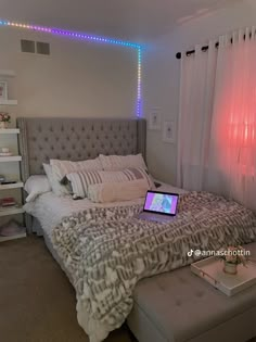 a laptop computer sitting on top of a bed in a room with white walls and curtains