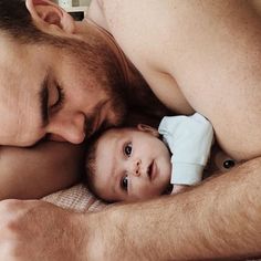 a man holding a baby in his arms while laying on top of a white blanket