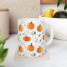 a white mug with orange pumpkins on it next to some lemons and other fruit