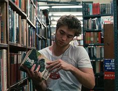 a man reading a book in a library with lots of bookshelves behind him