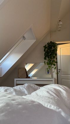 a white bed sitting under a window next to a plant in a vase on top of a dresser