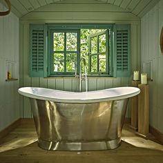 an old fashioned bathtub in a bathroom with green shutters and wood flooring