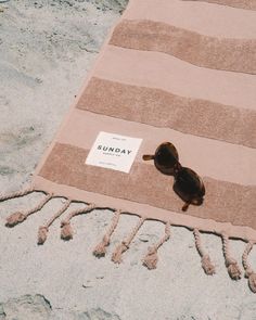 a towel with sunglasses on it laying on the beach next to a sign that says sunday