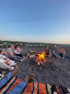 a group of people sitting around a campfire on top of a sandy beach next to the ocean