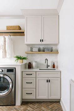 a washer and dryer in a small room with white cabinets, wood flooring and open shelving