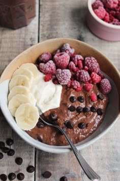 a bowl filled with chocolate pudding, bananas and raspberries on top of a wooden table