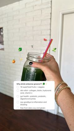 a person holding up a green smoothie in front of a white brick wall