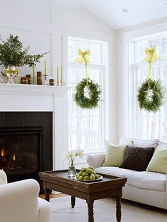 a living room with white furniture and wreaths on the fireplace mantel above it