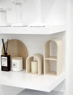 shelves with candles and other items on them in a white room or office space,