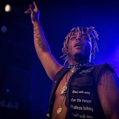 a man with dreadlocks standing in front of a microphone and holding his hand up