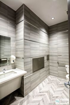 a bathroom with grey and white tiles on the walls, toilet paper dispenser