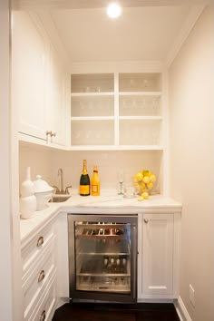 a small kitchen with white cabinets and stainless steel oven in the corner, along with wine bottles on the counter