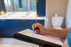 a person writing on a notepad in a bathroom with a sink and toilet behind them