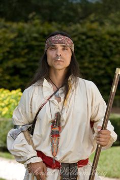 a man dressed in native american clothing holding a stick