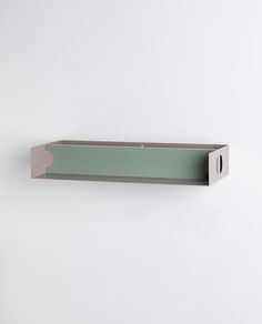 a white wall mounted shelf on the side of a wall with a light green box attached to it