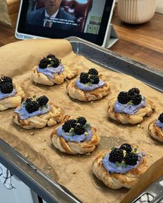 small pastries with blackberries are on a baking sheet in front of a laptop