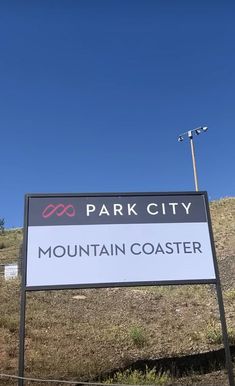 a sign for the park city mountain coaster in front of a grassy hill and blue sky