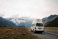 a van parked on the side of a road in front of snow capped mountain peaks