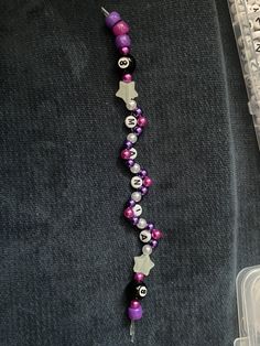 a purple and white beaded necklace with silver beads on it's end, next to a clear plastic container