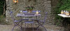 an outdoor table and chairs with candles on them in front of a stone wall, surrounded by greenery