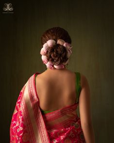 a woman wearing a pink and green saree with flowers in her hair, back view