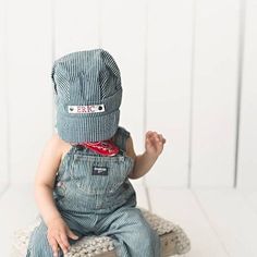 a baby sitting on top of a wooden stool wearing a blue and white striped jumpsuit