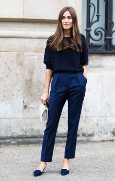 a woman in black shirt and blue pants standing on the street with her hands in her pockets