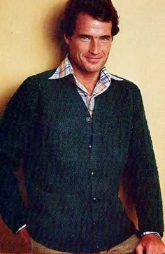 a man standing in front of a yellow wall wearing a green sweater and tan pants