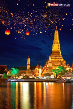 many lanterns are floating in the air over water at night with buildings and lights reflecting on the water