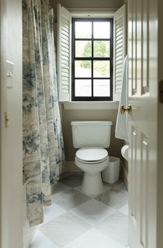 a white toilet sitting next to a window in a bathroom under a curtained window