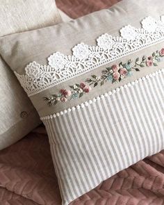 two pillows on a bed with white lace trimmings and pink flowers in between them