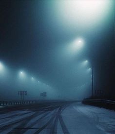 an empty road with street lights in the fog on a cold day at night time