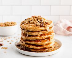 a stack of pancakes topped with granola on a plate next to a bowl of oatmeal