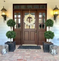 the front door is decorated with wreaths and potted trees