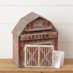 a red barn shaped mailbox sitting on top of a wooden table next to a white wall