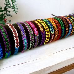 a bunch of colorful bracelets sitting on top of a wooden table next to a potted plant