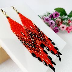 red and black beaded earrings sitting on top of a white table next to flowers