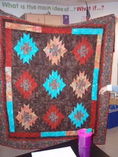 a large quilt is on display in an office space with purple vases next to it