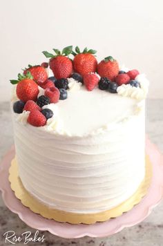 a white cake topped with berries and blueberries on top of a pink platter