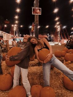 two women are posing with pumpkins in the middle of a hay field at night