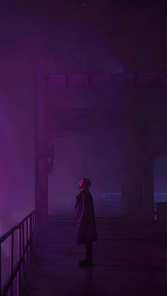 a person standing on a bridge in the dark with purple light coming from behind them