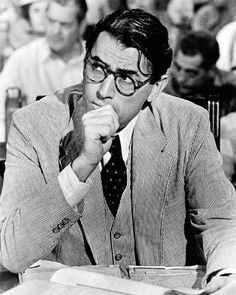 black and white photograph of man in suit sitting at desk with papers, reading glasses