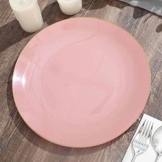 a pink plate sitting on top of a wooden table next to a candle and two white candles