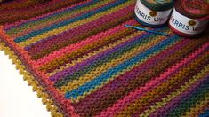 two balls of yarn sitting on top of a multicolored crocheted blanket