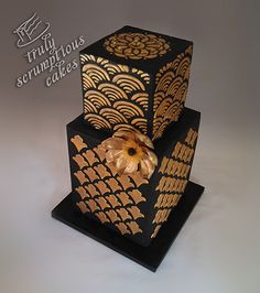 a three tiered black and gold cake with an orange flower on the top layer