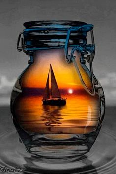 a glass jar filled with water and a sailboat floating in the ocean at sunset