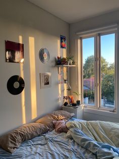 an unmade bed sitting in front of a window next to a wall with pictures on it