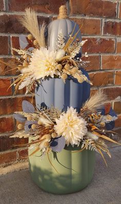 a blue and green vase with dried flowers in it sitting on the ground next to a brick wall