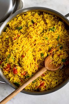 a large pot filled with yellow rice next to two silver pans and wooden spoon