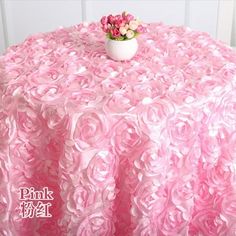 a round table covered in pink ruffled cloth with a vase of flowers on top